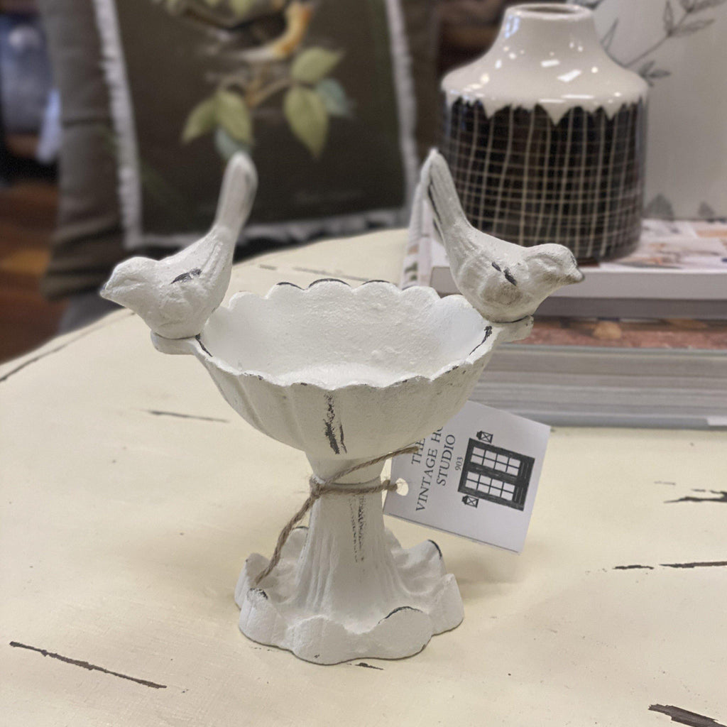 Cast iron bird bath pedestal with two small birds on edge of bowl in antique white finish with distressed details.